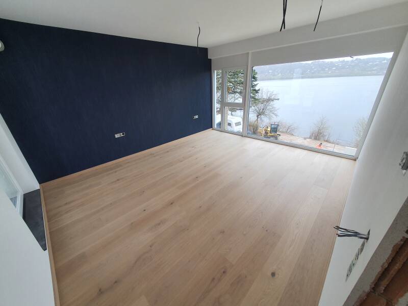 The same living room in Germany with wood-look flooring laid and a dark blue painted wall